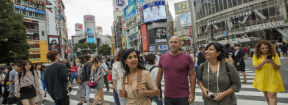 Eine junge Frau geht in Tokio über eine Zebrastreifen mit vielen anderen Menschen auch
