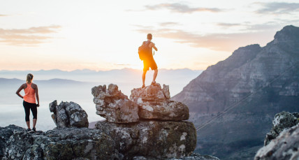 Eine Frau und ein Mann stehen auf Felsen und schauen in die Weite bei Sonnenuntergang