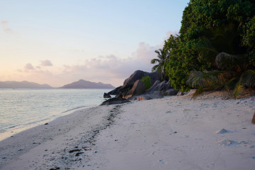 Sonnenuntergang am Strand mit Blick auf Granitfelsen und Palmen
