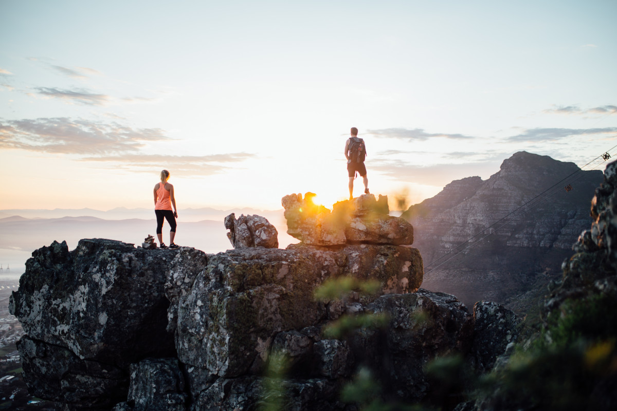 Zwei Personen sehen sich den Sonnenuntergang auf dem Berggipfel in Südafrika an