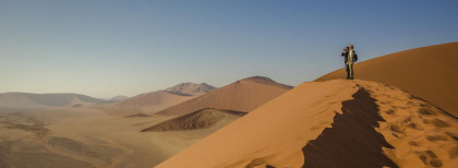 Zwei Leute schauen mit einem Fernglas die Dünen der Wüste an 