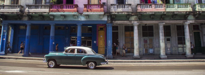 Fahrender Oldtimer auf den Straßen Kubas vor einer bunten Häuserfassade