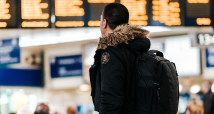 Mann mit Rucksack am Flughafen schaut auf die Abflugtafel