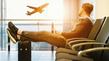 Mann der aus einem Fenster auf einen Flugzeug mit seinen Beinen auf seinen Koffer