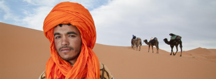 Ein Mann mit einem gelben Kopftuch mit drei kämmeln in einer Wüste 