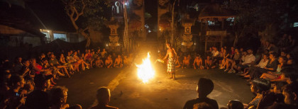 Lagerfeuer mit vielen Menschen die drumherum sitzen und einer gießt Öl und in das Feuer