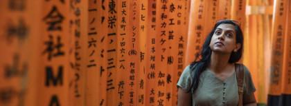 Eine Frau die durch einen Tunnel aus orangenen Stäben mit japanischer Schrift geht