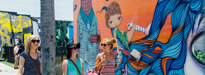 Drei Frauen gehen lächelnd an einer bunt besprayten Wand in Florida entlang