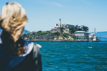 Blonde Frau blickt auf "The Rock", das ehemalige Hochsicherheitsgefängnis Alcatraz an einem sonnigen Tag