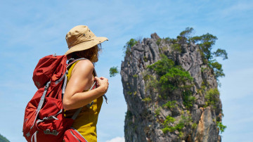 Eine Frau mit Rucksack mit Blick auf einen großen Felsen