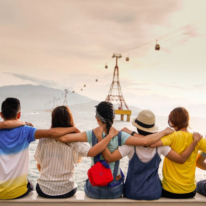 Eine Gruppe von jungen Menschen blicken Arm in Arm aufs Meer