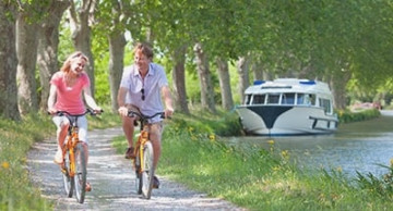 Zwei Menschen auf dem Fahrrad auf einem Weg am Fluss vorbei